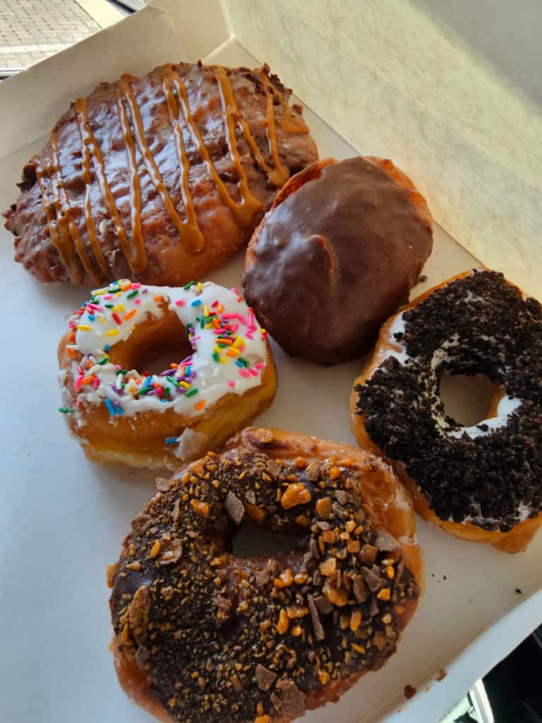 Box of city donuts with a Butterfinger donut, Oreo Donut, Boston Cream Pie Donut, Sprinkle donut, and caramel apple fritter