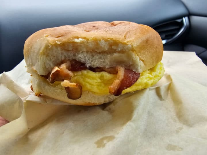 Bacon egg and cheese breakfast sandwich on a piece of parchment paper being held