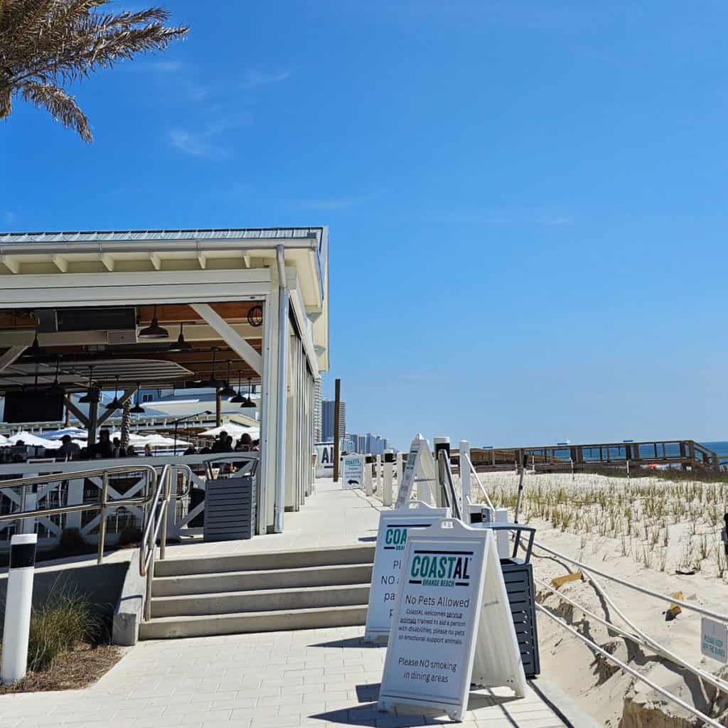 Outdoor dining with a Coastal Orange Beach sign and the beach with boardwalk