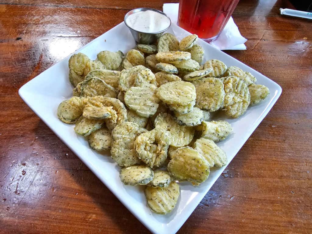 White plate with fried pickles piled on it with a side of ranch