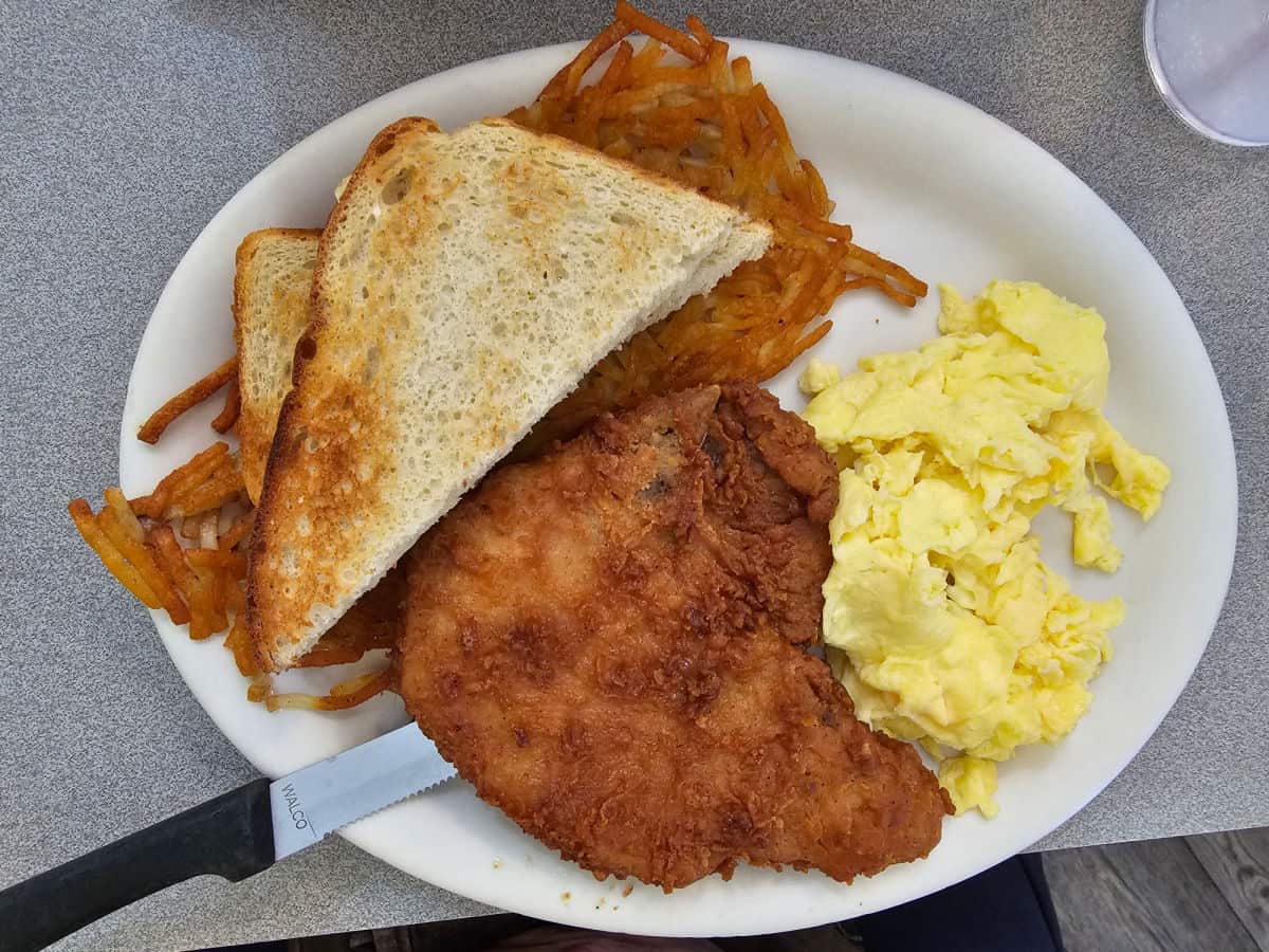 fried pork chop next to scrambled eggs, hashbrowns and two slices of toast