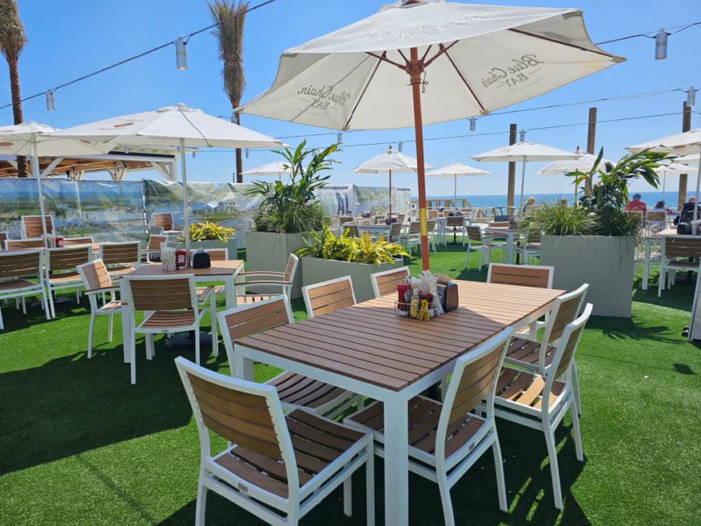 outdoor dining tables with white umbrellas on green AstroTurf with blue skies
