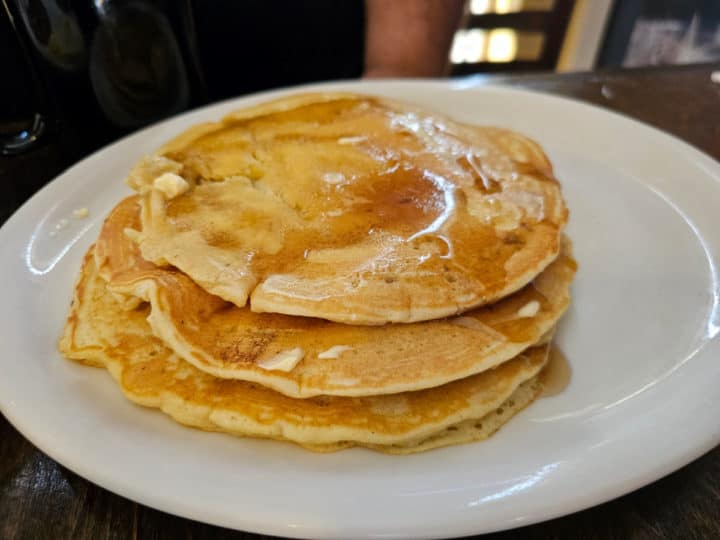 Stack of three pancakes with syrup on a white plate