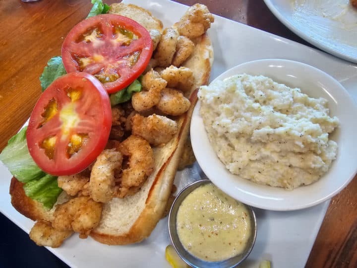 Shrimp PoBoy with tomato and lettuce next to gouda grits in a white bowl
