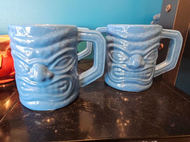 Two blue tiki faced coffee mugs on a counter