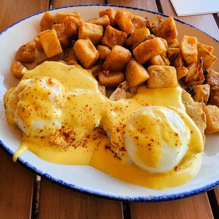 Eggs benedict with potatoes on a white plate