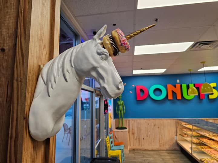 Unicorn head with donuts on its horns and donuts on the wall behind 