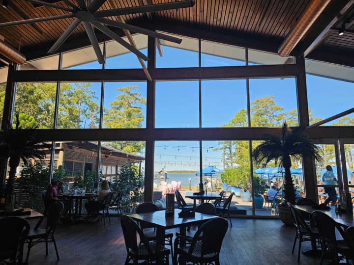water views through a large glass window with tables and chairs near it. 