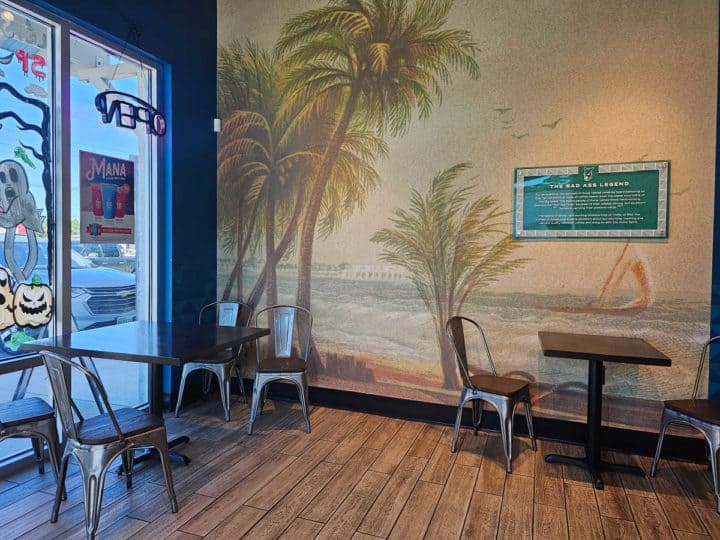 Tables and chairs near a tropical mural on the wall with palm trees