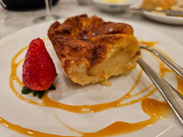 Bread pudding on a white plate with a strawberry and caramel swirl