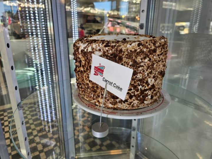complete carrot cake with small sign in a glass bakery case