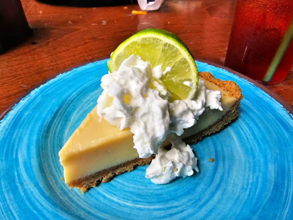 Slice of key lime pie with whipped cream and a lime circle on a blue plate