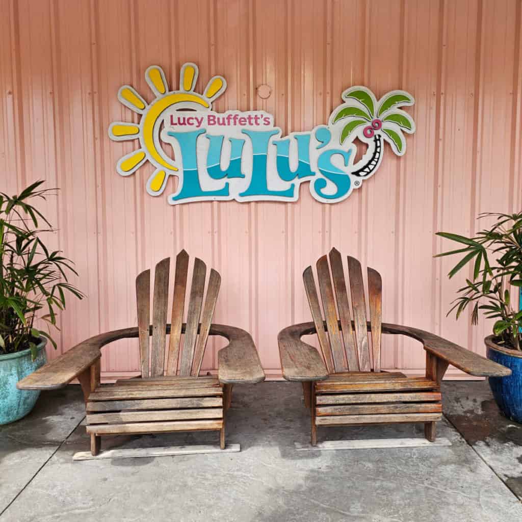 Lucy Buffett's LuLu's sign over 2 Adirondack Chairs with plants next to them