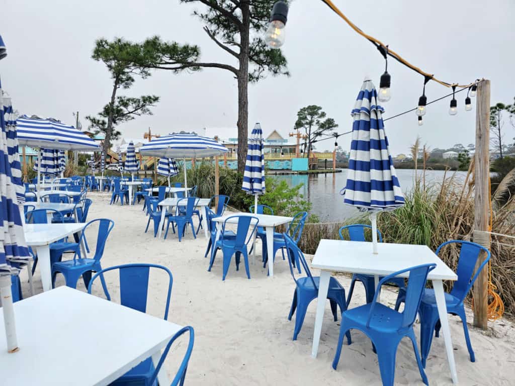 Outdoor Seating with white tables, blue chairs, and striped umbrellas with water in the background 
