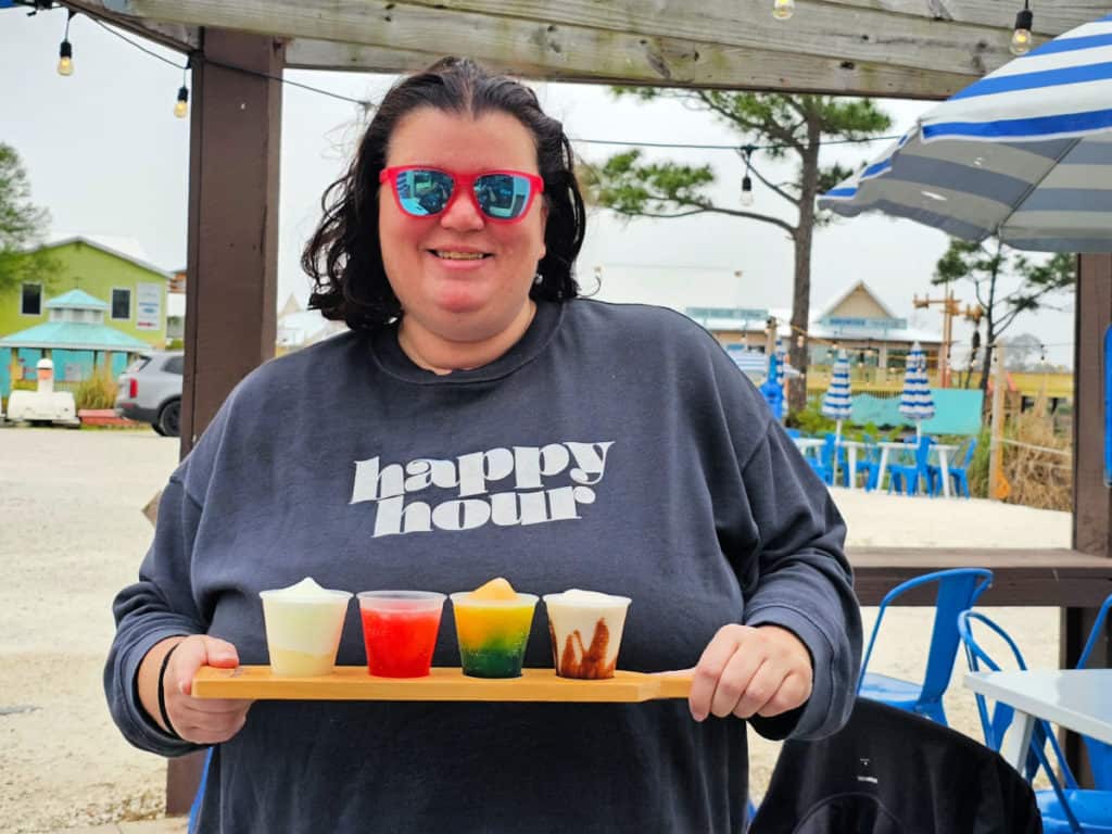 Tammilee wearing a Happy Hour sweatshirt holding a daiquiri board with 4 drinks