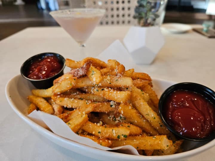 truffle fries in a white bowl with two small ramekins of ketchup next to a lavender martini