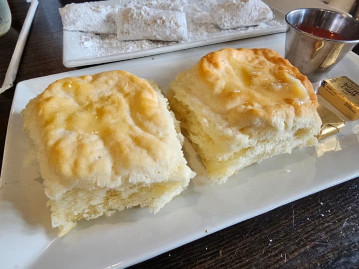 Two large biscuits on a white platter with butter and a jam container