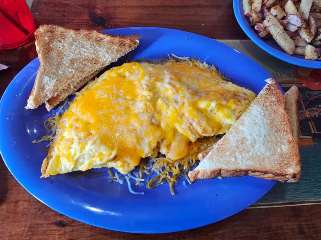 Cheese omelet with white toast on a blue plate next to a bowl of potatoes