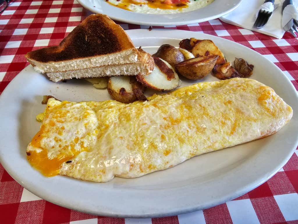 Cheese omelet on a white plate with breakfast potatoes and toast at The Ugly Diner