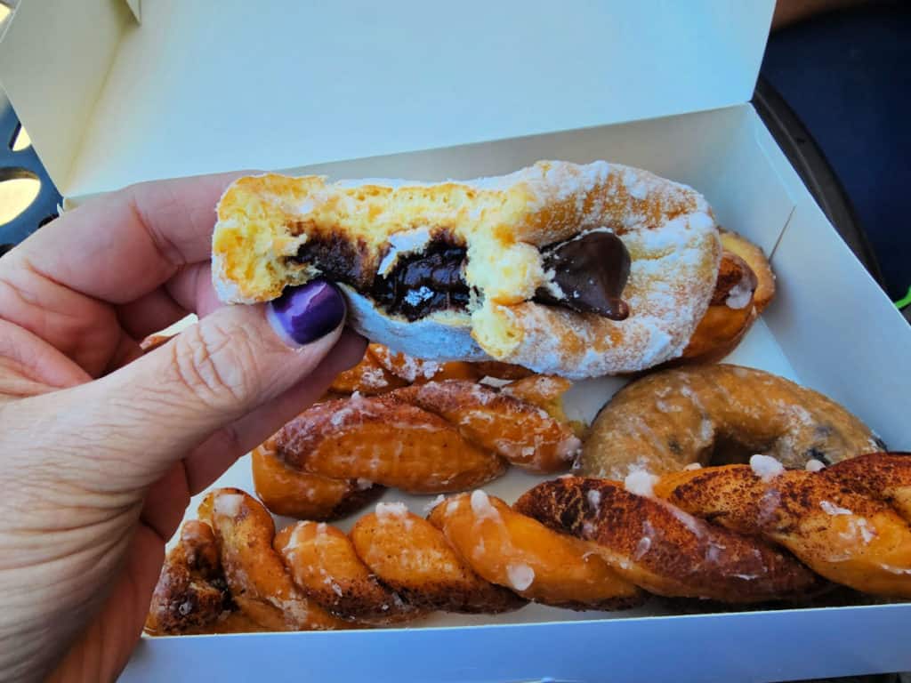 Hand holding a chocolate filled donut over a box of doughnuts