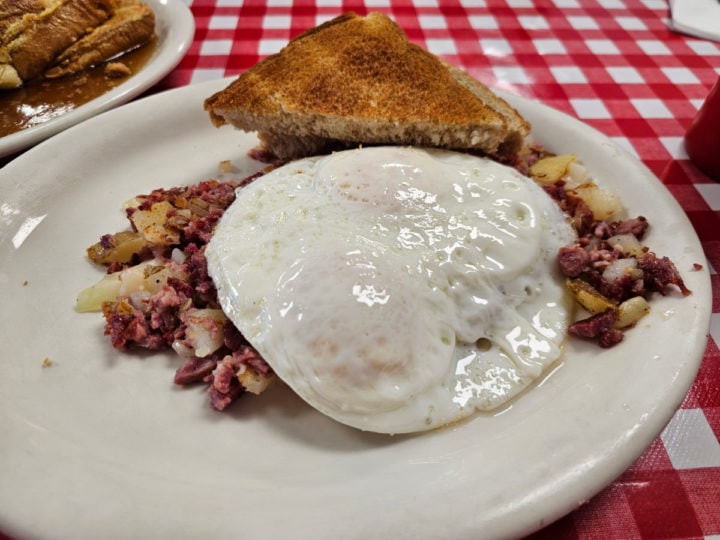 corned beef and hash with an over medium egg on a white plate with toast