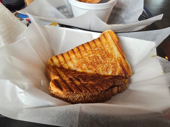 Grilled cheese sandwich in a paper lined container on a table near soup