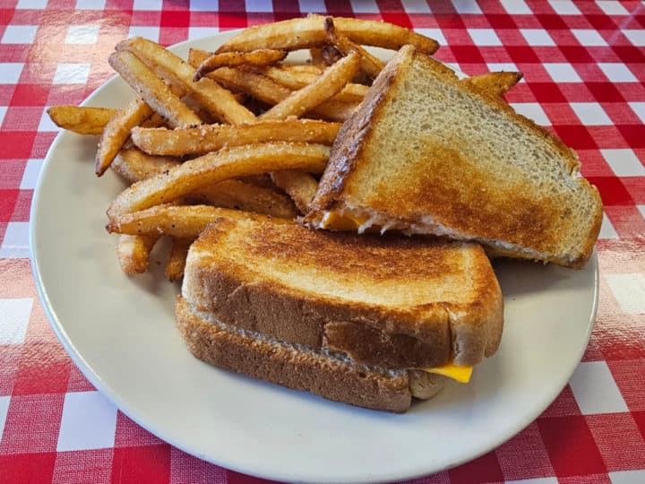 Grilled cheese and fries on a white plate sitting on a red and white checkered tablecloth