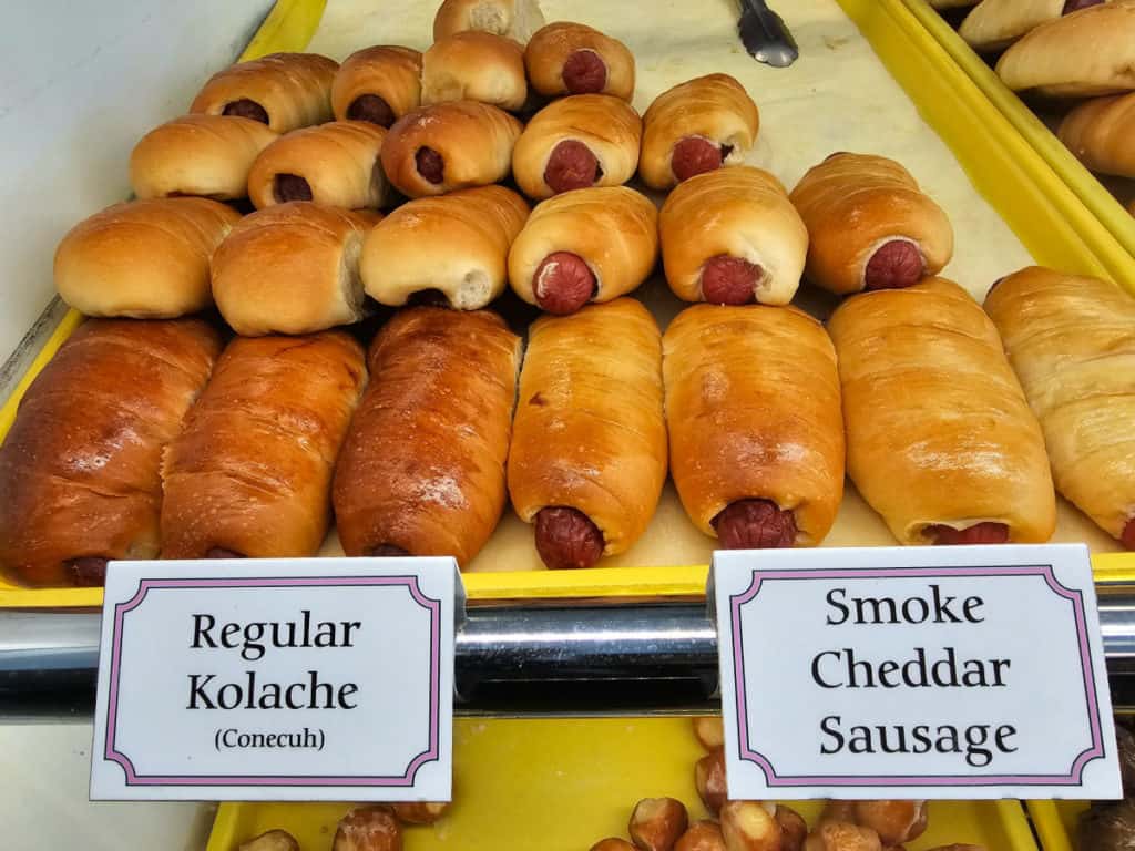 Regular Kolache and Smoke Cheddar Sausage sign in front of a yellow tray filled with kolaches