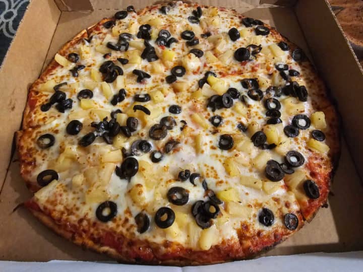 Pineapple and black olive pizza in a cardboard delivery box