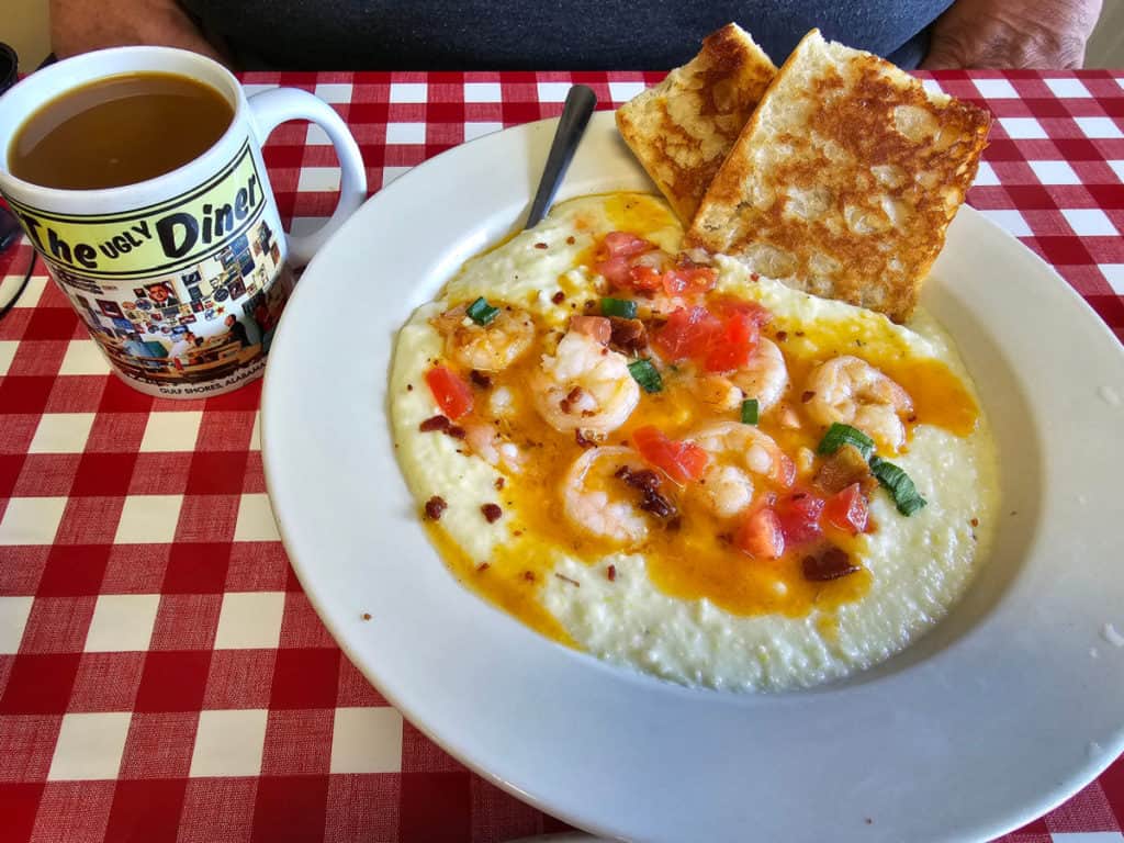 Shrimp and grits in a white bowl with two slices of bread next to an Ugly Diner mug