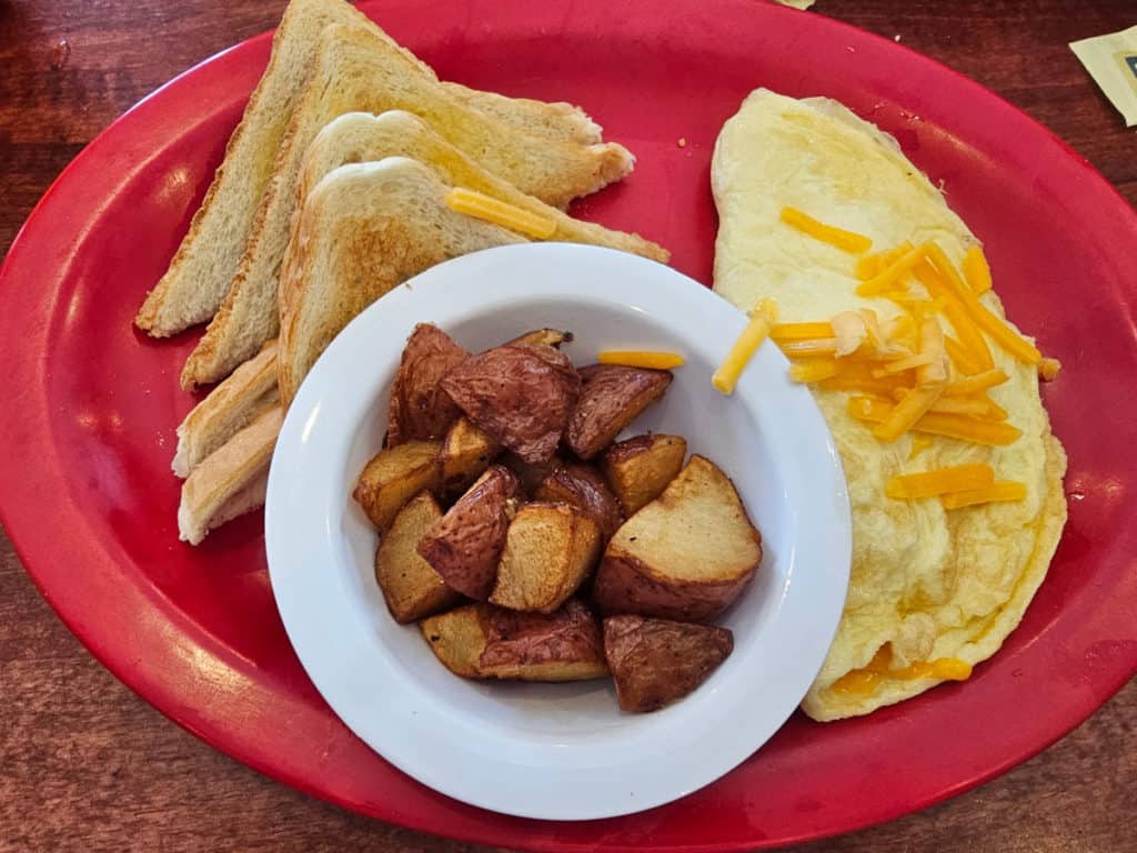 cheese omelet with a white bowl of potatoes and slices of toast on a red plate