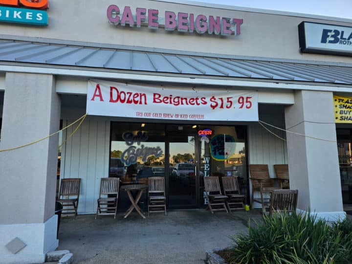 Cafe beignet sign with a dozen beignets over the entrance door with wooden chairs