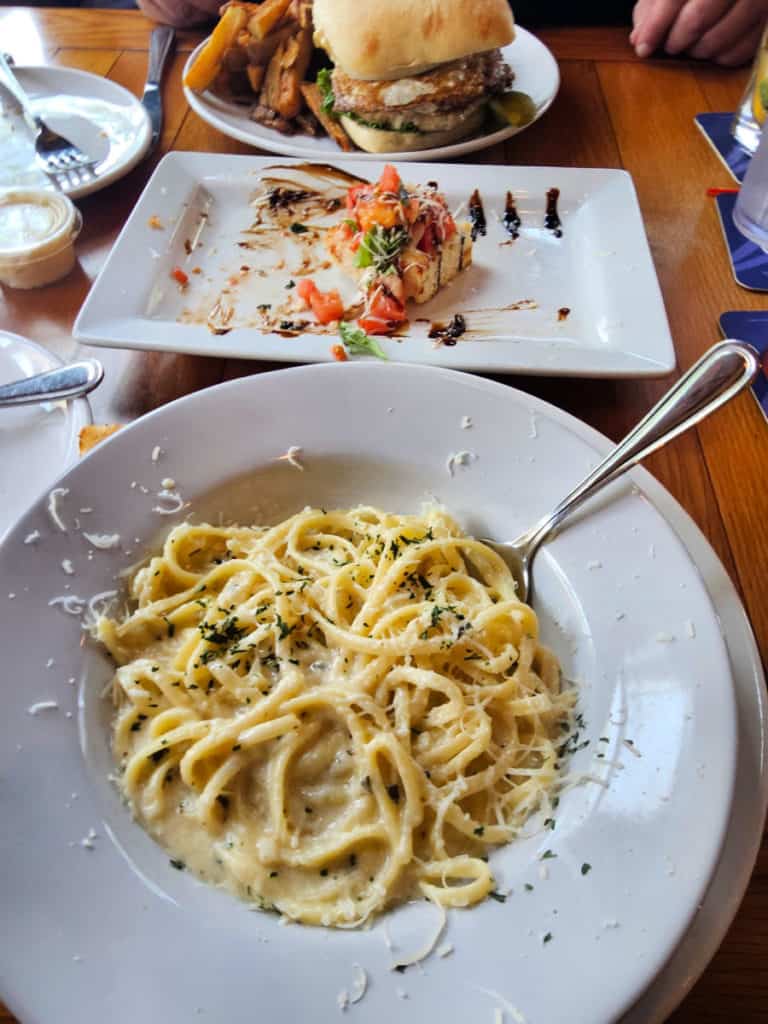 Fettuccine alfredo on a white plate next to bruschetta and a burger at locals fairhope