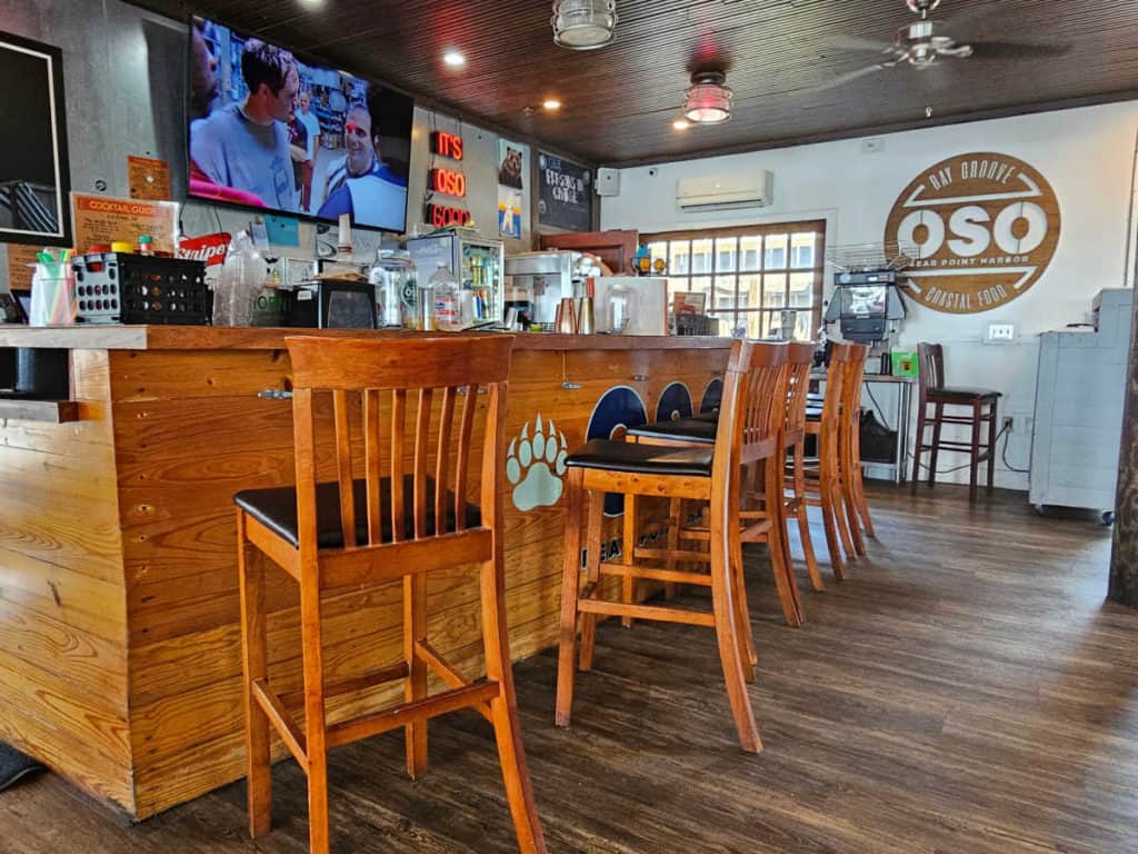 Indoor bar seating with high top chairs and a wooden bar next to TVs at Oso Orange Beach