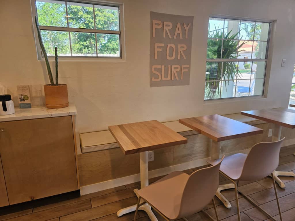 interior seating with wooden bench and tables at Foam Coffee, art saying Pray for Surf