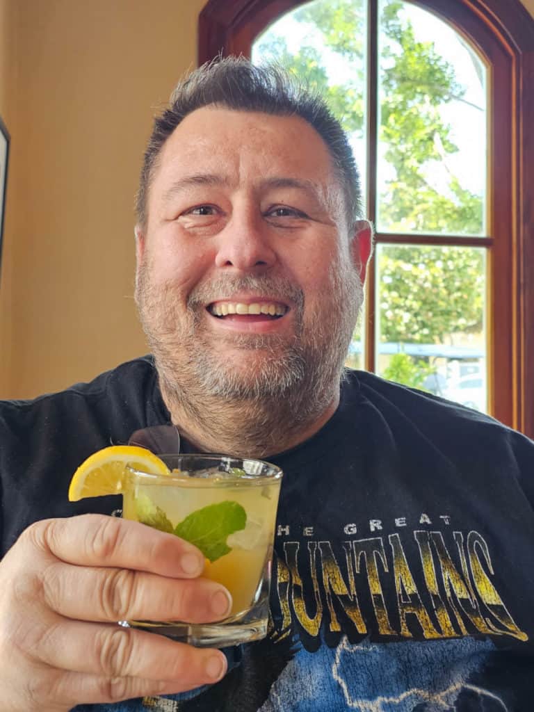 John holding a bourbon cocktail with lemon wedge and mint
