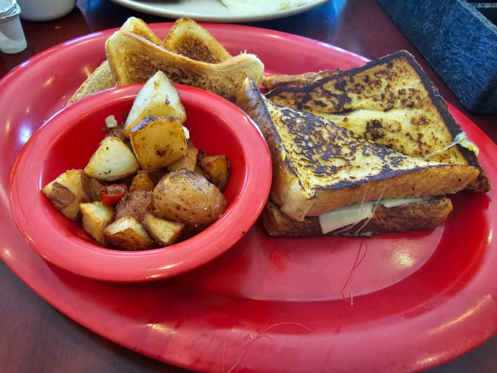 French toast breakfast sandwich next to a bowl of potatoes and toast