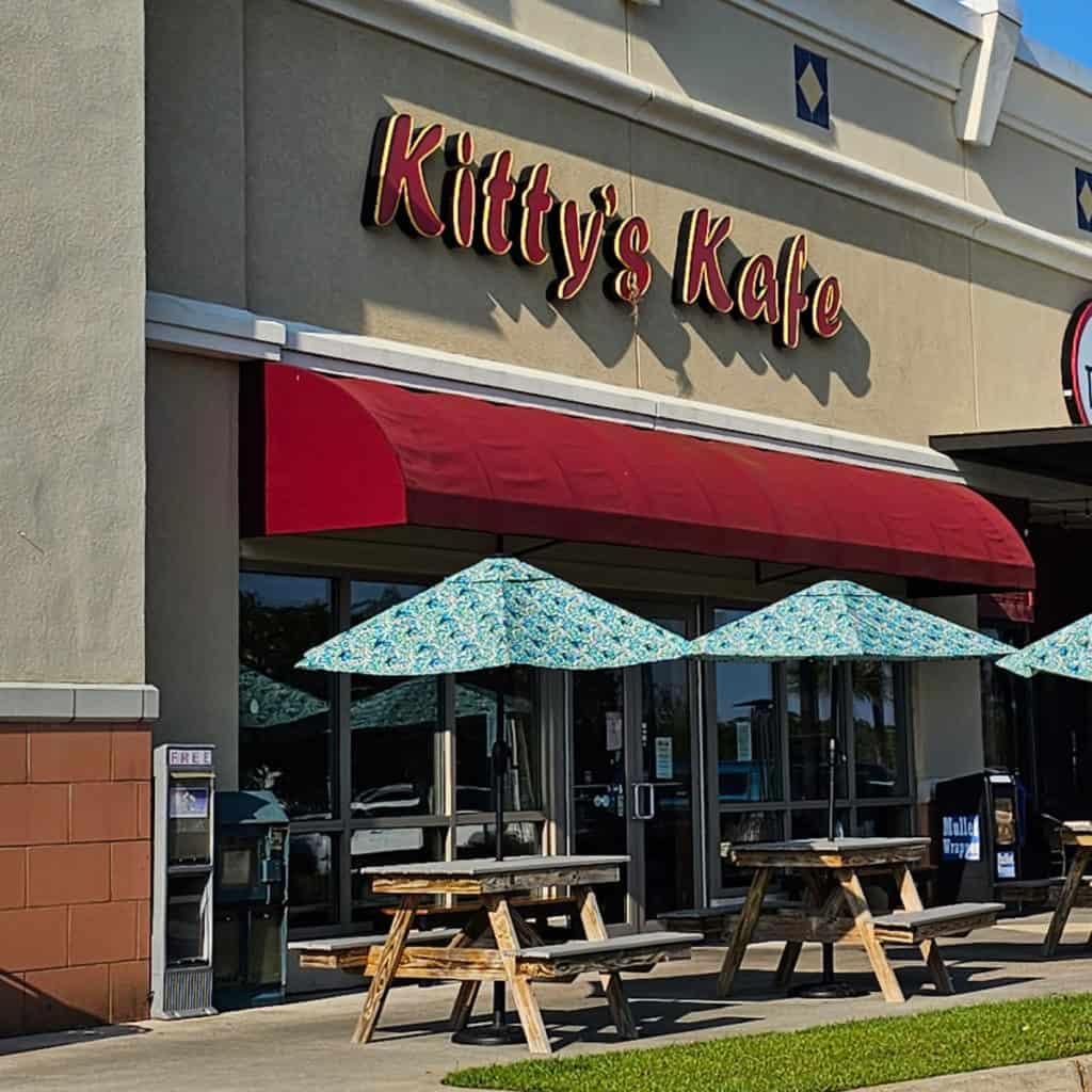 Exterior of Kitty's Kafe with red awning and picnic tables with umbrellas