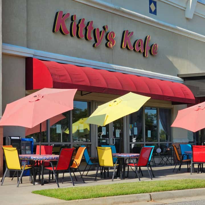 Kitty's Kafe red sign over a red awning, multiple tables with red and yellow umbrellas