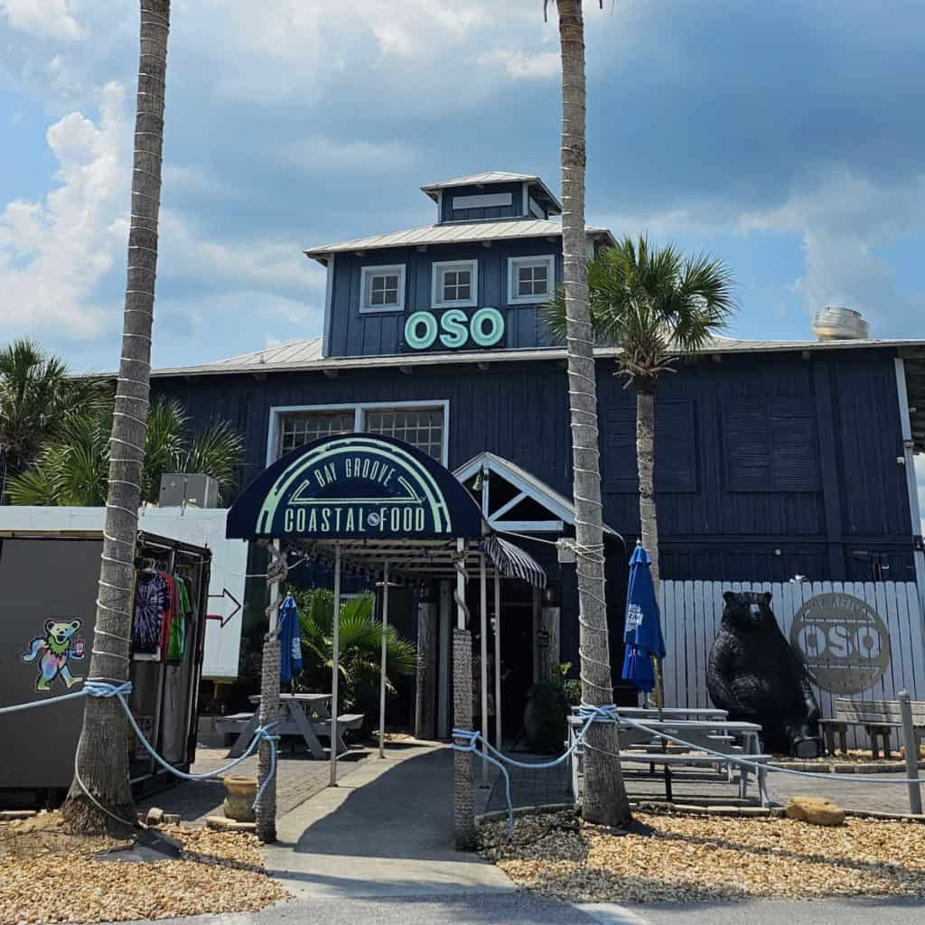 OSO restaurant with a large bear statue, picnic tables, and palm trees
