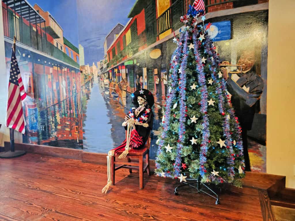 skeleton figurine on a chair next to a patriotic Xmas tree in front of a mural at Ginny Lane Bar and Grill