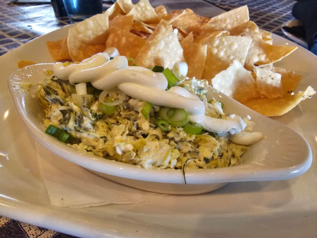 Spinach Artichoke dip in a white bowl next to tortilla chips