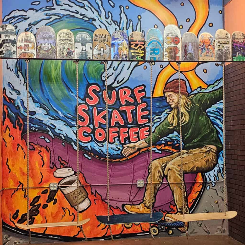 Surf Skate Coffee mural with a skateboarder painted behind hanging skateboard swings