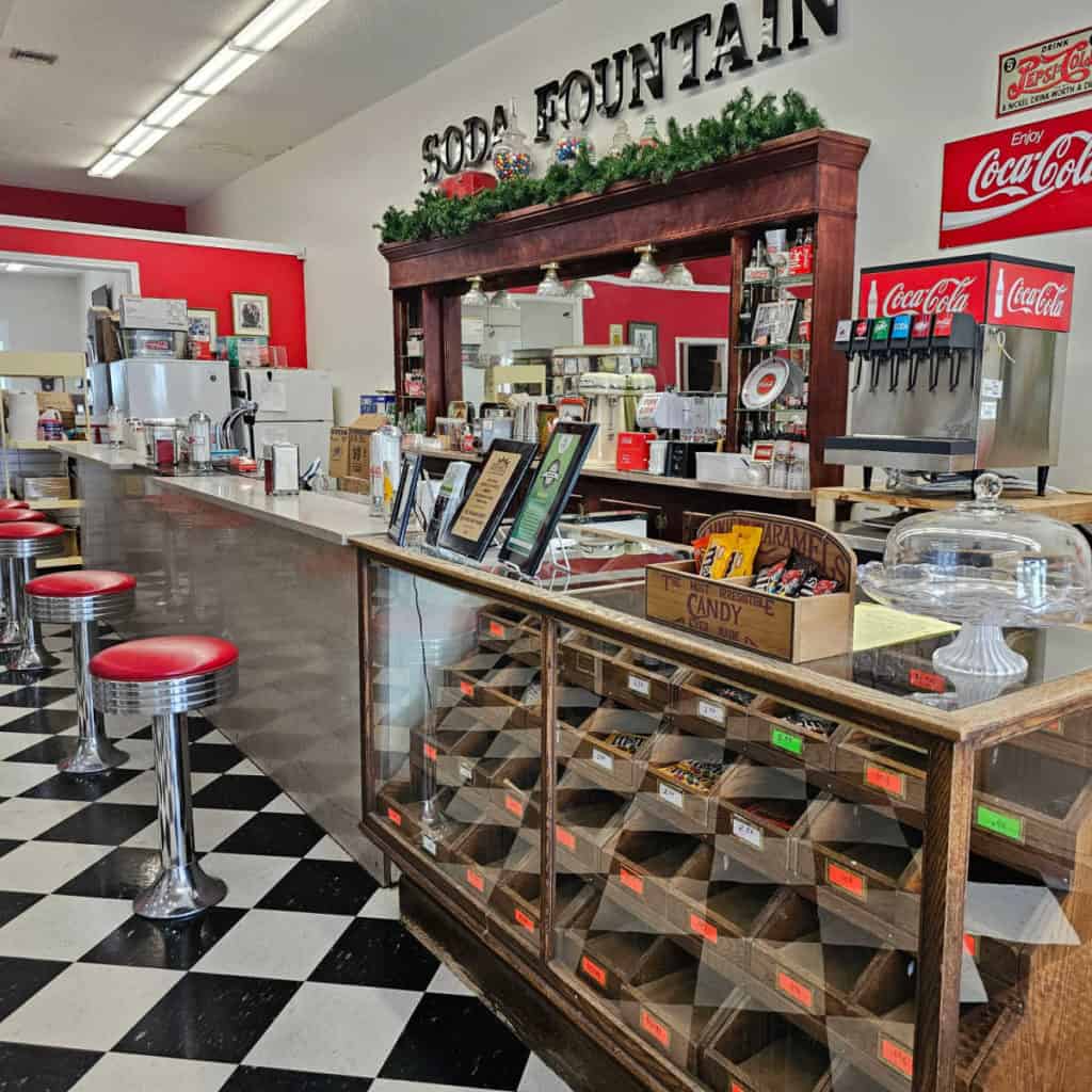 Soda fountain sign above a bar with red stools and a coke machine
