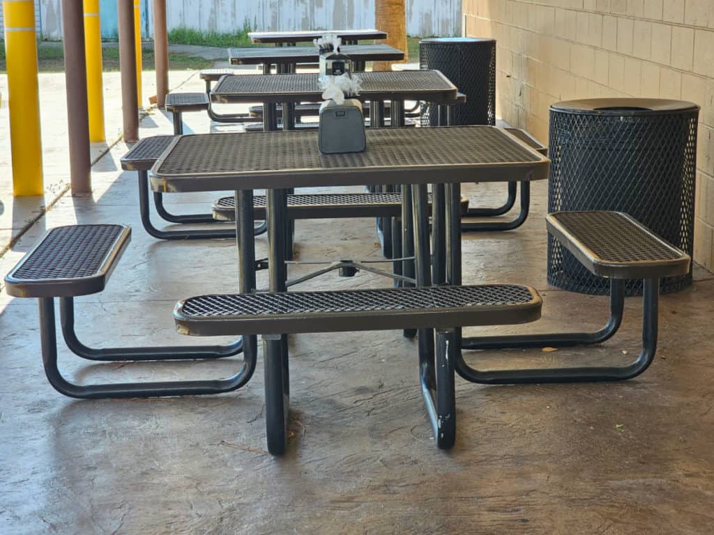 Outdoor black tables with benches attached and a garbage can