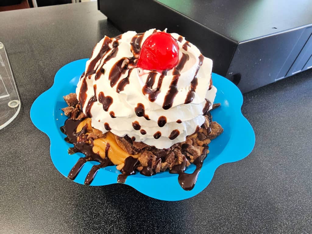 blue sundae cup filled with ice cream, whipped cream, chocolate drizzle and a cherry on top
