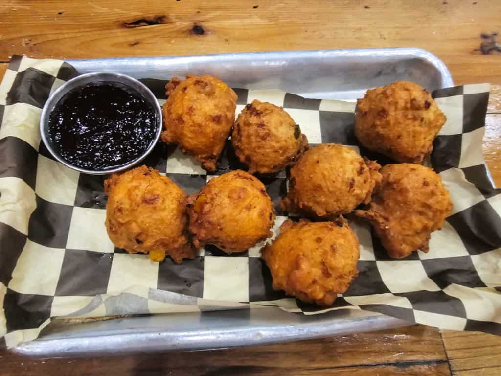 Pimiento Hushpuppies with housemade blueberry pepper jelly on a checkered paper in a silver tray
