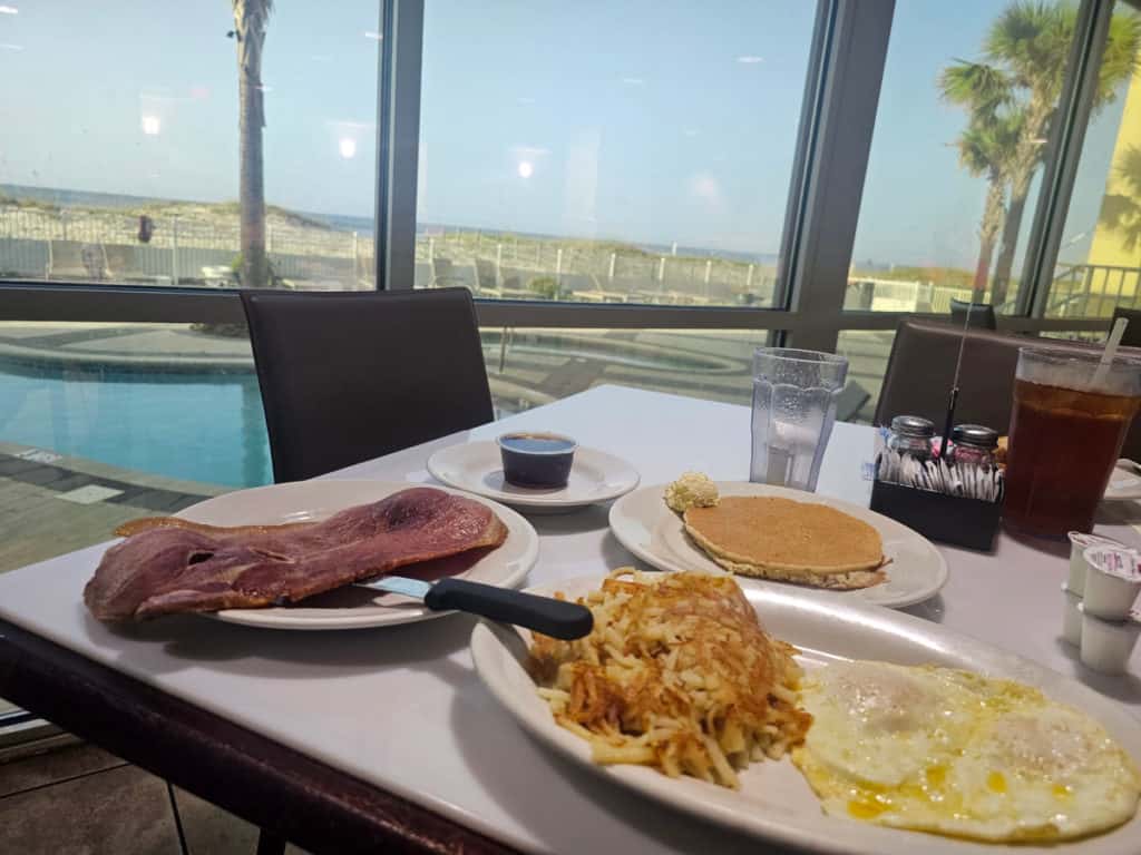 ham, hashbrown, fried eggs and pancakes on a white plate with a view of the Gulf of Mexico
