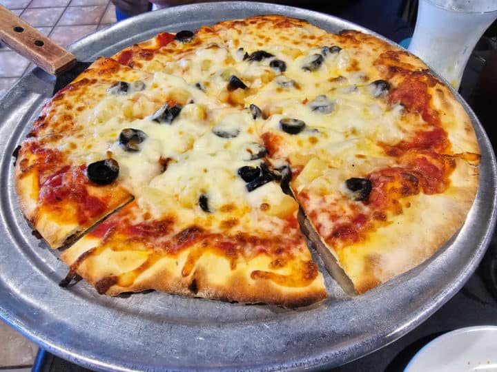 black olive and pineapple thin crust pizza on a pizza pan