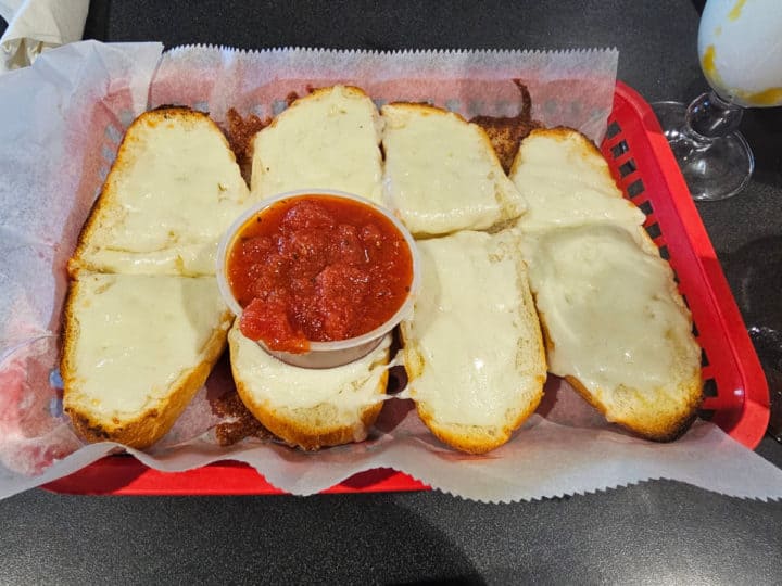cheese bread with a container of marina sauce on a red tray